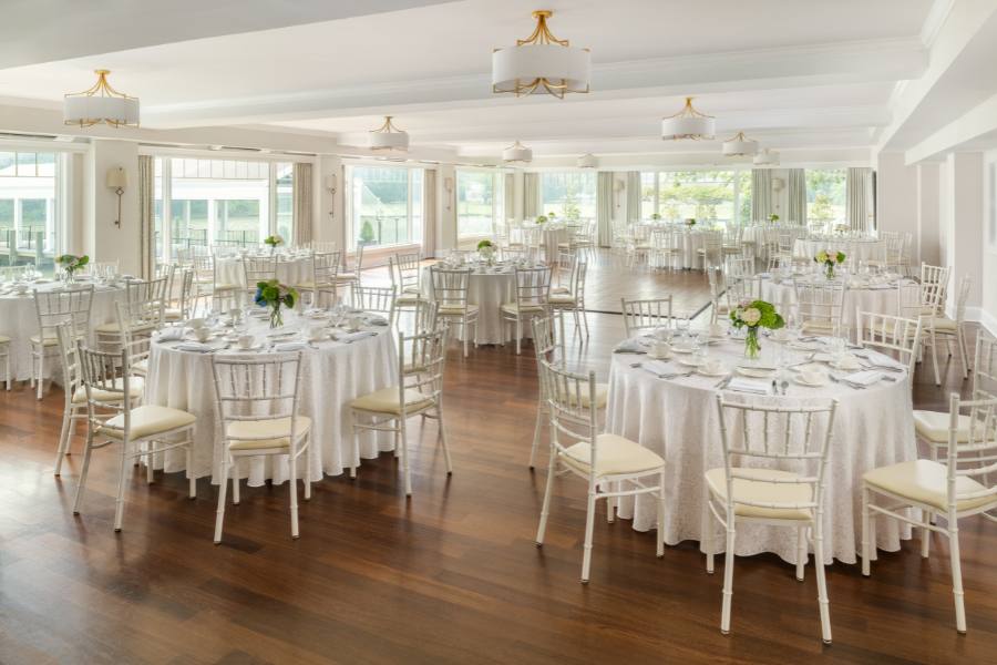 Wedding reception space with several round tables and white chairs