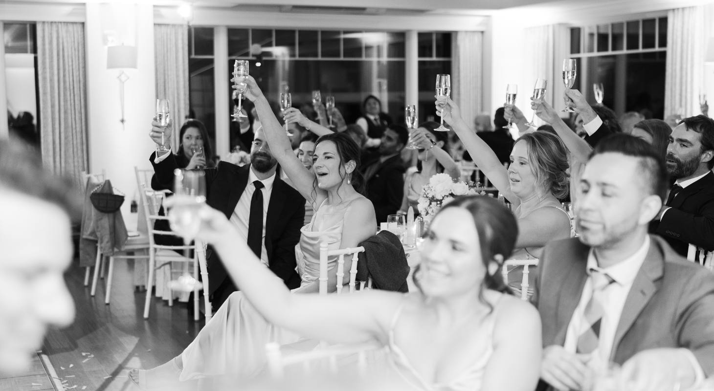 People holding up champagne glasses for a toast at a wedding in black and white